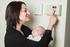 A woman holding a baby while adjusting heating controls
